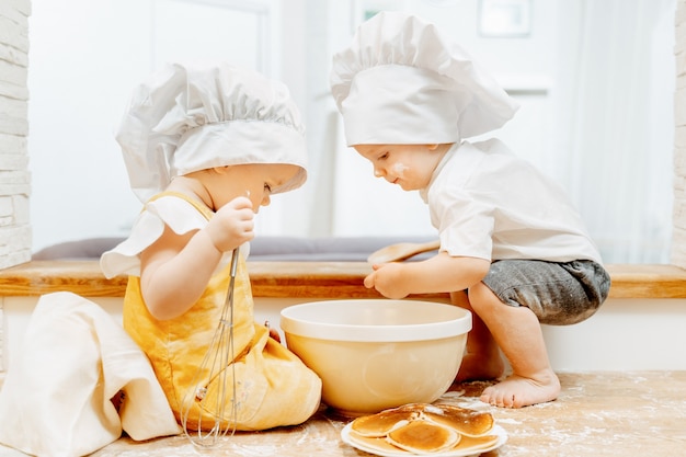 Vue latérale des enfants mignons jumeaux garçons et une fille en chapeaux de cuisinier préparer la pâte