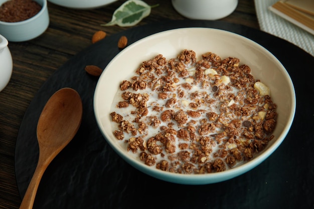 Vue latérale de la farine d'avoine avec du lait de noix et des amandes avec une cuillère en bois sur un dessous de plat sur fond de bois