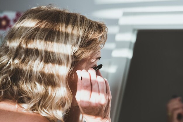 Photo vue latérale d'une femme appliquant du mascara à la maison