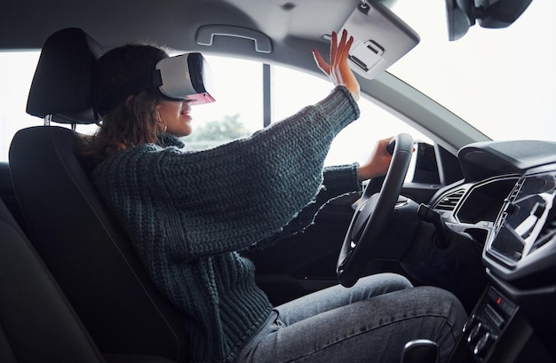 Vue latérale d'une femme dans des lunettes de réalité virtuelle assise à l'intérieur d'une voiture moderne.