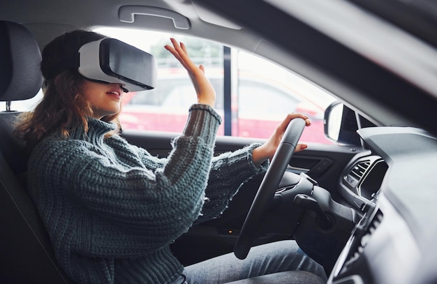 Photo vue latérale d'une femme dans des lunettes de réalité virtuelle assise à l'intérieur d'une voiture moderne.