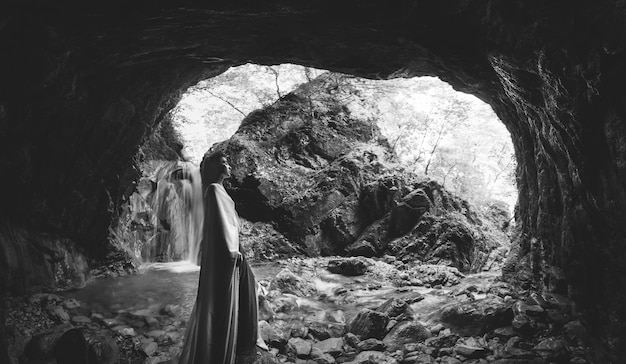 Photo vue latérale d'une femme debout dans une grotte près d'une cascade