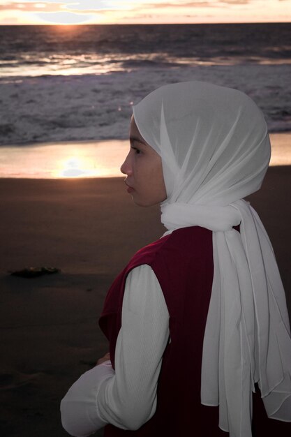 Photo vue latérale d'une femme debout sur la plage au coucher du soleil