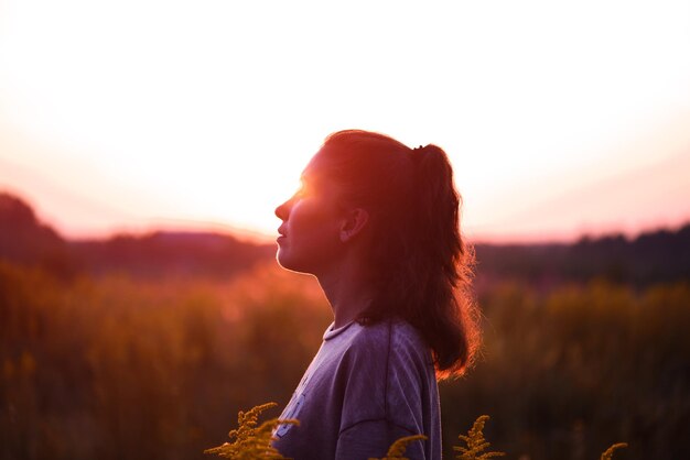 Photo vue latérale d'une femme détournant son regard alors qu'elle se tient près des plantes contre le ciel au coucher du soleil