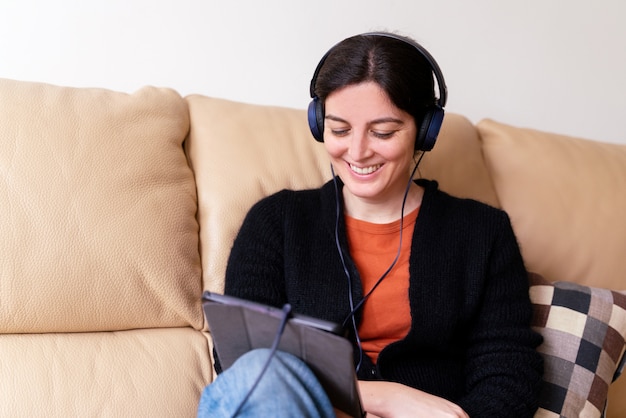 Vue latérale d'une femme joyeuse avec un casque appelant un ami malade avec un appareil électronique. Concept de distance sociale en isolement de quarantaine à la maison.