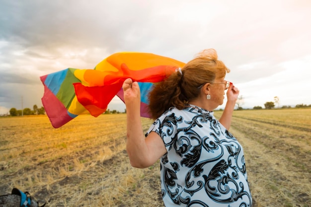 Vue latérale d'une femme mûre tenant un drapeau arc-en-ciel au coucher du soleil