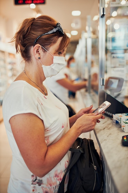 Photo vue latérale d'une femme portant un masque en utilisant un téléphone portable au supermarché