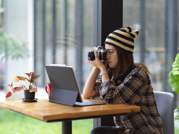 Vue latérale de la femme prenant photo appareil photo numérique blanc alors qu'il était assis à une table basse avec un ordinateur portable au café