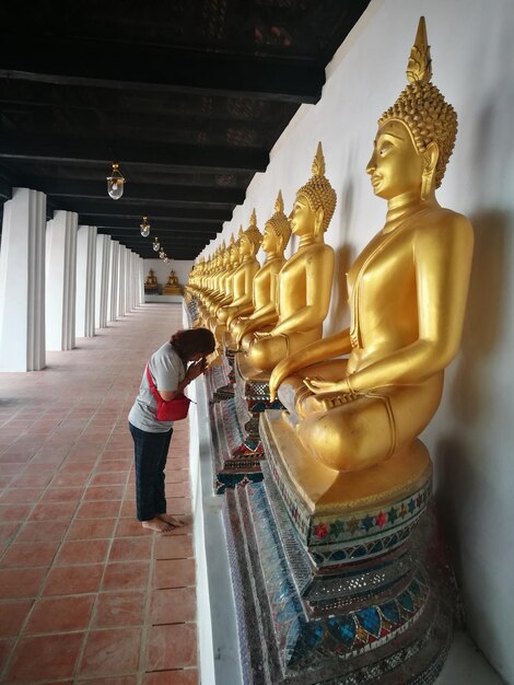 Photo vue latérale d'une femme priant devant la statue d'or du bouddha dans le temple