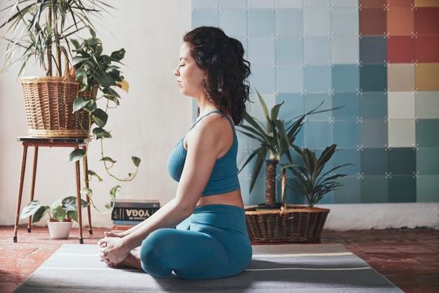 Vue latérale d'une femme qui médite assise près des plantes en pot à la maison