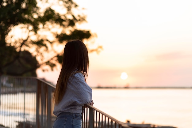 Photo vue latérale femme regardant le coucher du soleil