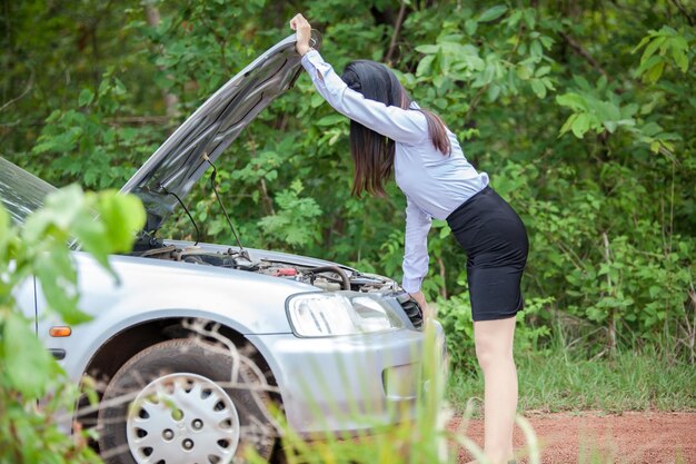 Vue latérale d'une femme regardant le moteur d'une voiture sur un trottoir