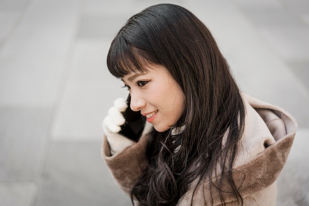 Photo vue latérale d'une femme souriante parlant au téléphone à l'extérieur