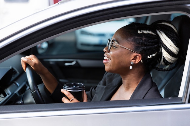 Vue latérale d'une femme souriante prenant un café à l'intérieur de sa voiture