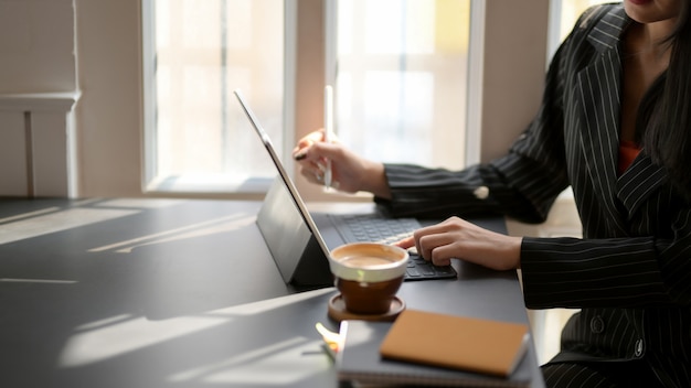 Vue latérale d'une femme tapant sur une tablette numérique sur un tableau noir dans un lieu de travail confortable