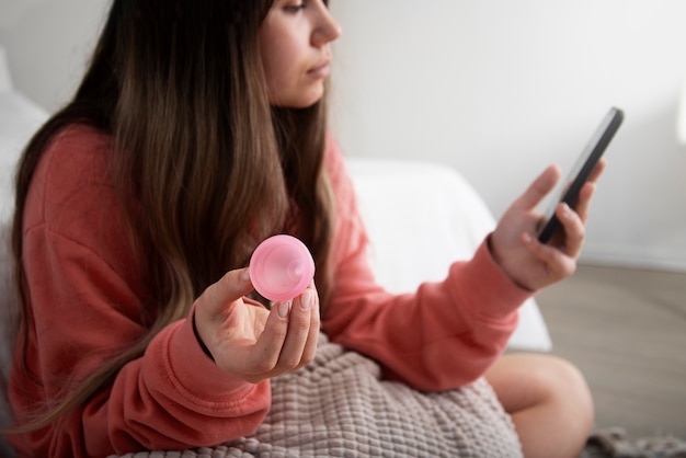 Vue latérale femme tenant une coupe menstruelle et un téléphone