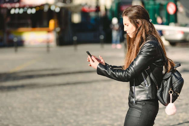 Vue latérale d'une femme utilisant un smartphone dans la rue