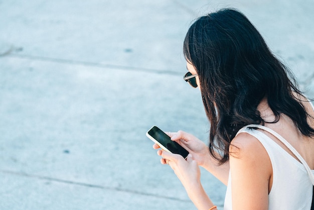 Vue latérale d'une femme utilisant un smartphone dans la rue
