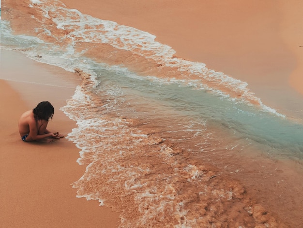 Vue latérale d'une fille sans chemise assise sur la plage