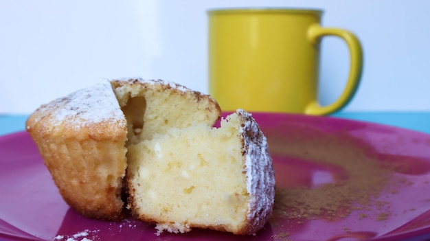 Vue latérale d'un fromage cottage saupoudré de sucre glace sur une plaque rose à côté d'une tasse de café ou de thé jaune. Dessert, un petit cupcake. biscuits blancs cuits au four avec une texture aérée. Espace de copie