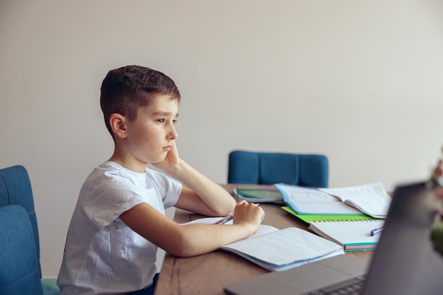 Vue latérale sur un garçon caucasien triste élève faisant ses devoirs et étant paresseux apprenant à la maison