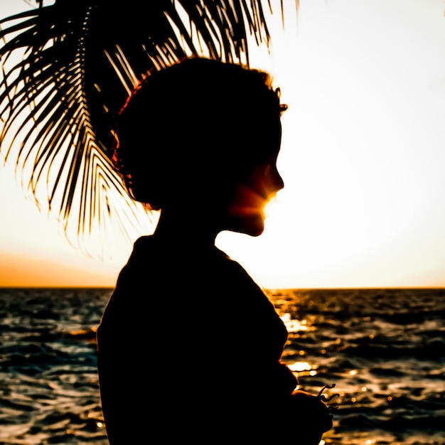 Photo vue latérale d'un garçon en silhouette sur la plage contre le ciel au coucher du soleil