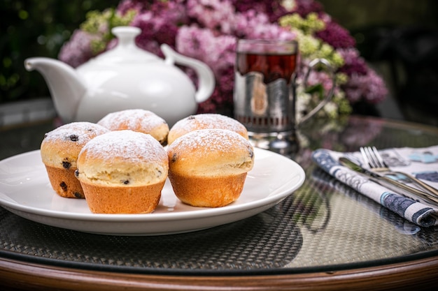 Photo vue latérale des gâteaux sur une assiette blanche et une théière blanche et un verre de thé avec fond de fleurs violettes