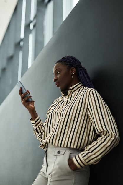 Vue latérale graphique portrait d'une femme d'affaires afro-américaine confiante tenant un smartphone en se tenant debout sur fond noir