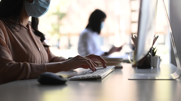 Vue latérale des graphistes féminins portant des masques médicaux et travaillant au bureau moderne