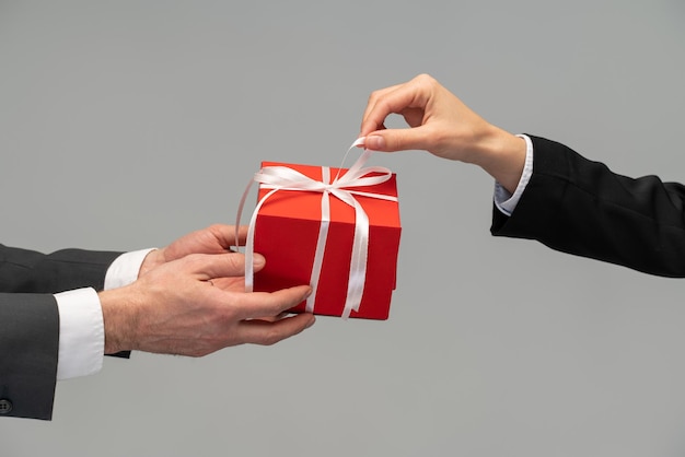 Vue latérale en gros plan d'une main masculine tenant une boîte-cadeau rouge avec un ruban donnant un cadeau sur le concept de bonus et de surprises de vacances Prise de vue en studio intérieure isolée sur fond gris