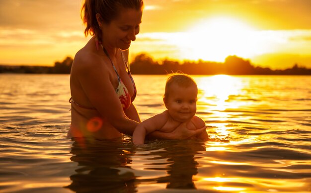 Vue latérale de l'heureuse mère caucasienne nageant avec petit bébé souriant mignon en mer