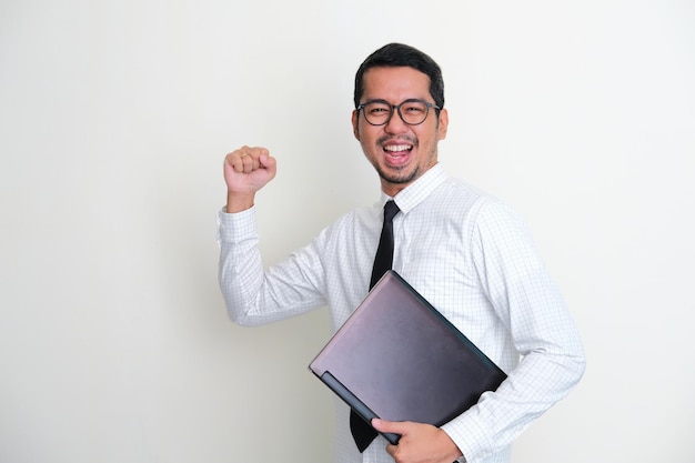 Vue latérale d'un homme d'affaires asiatique tenant un ordinateur portable tout en serrant le poing et montrant une expression confiante