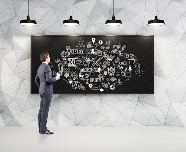 Vue latérale d'un homme d'affaires avec une tasse de café en papier regardant un grand croquis blanc d'équipe d'affaires dessiné sur un tableau noir. Motif mural géométrique. rendu 3d