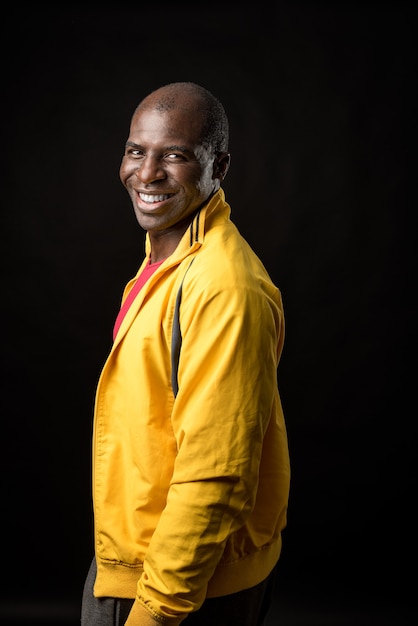 Vue latérale d'un homme afro-américain debout regardant la caméra et souriant sur fond noir