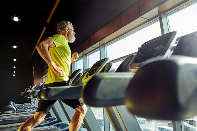 Vue latérale d'un homme d'âge moyen athlétique en tenue de sport s'exécutant sur un tapis roulant dans une salle de sport faisant du cardio