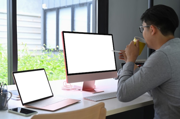 Vue latérale Homme asiatique buvant du café et travaillant avec des appareils modernes.