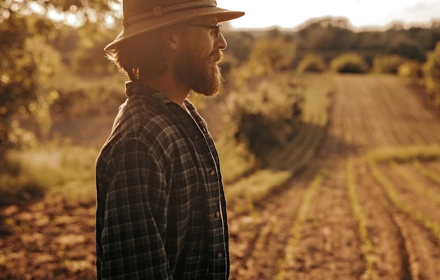 Photo vue latérale d'un homme barbu debout près de champ agricole labouré