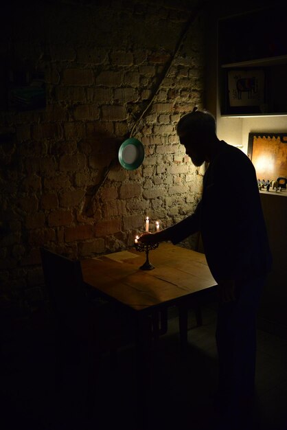 Vue latérale d'un homme contre le mur dans l'obscurité allumant des bougies dans un chandelier