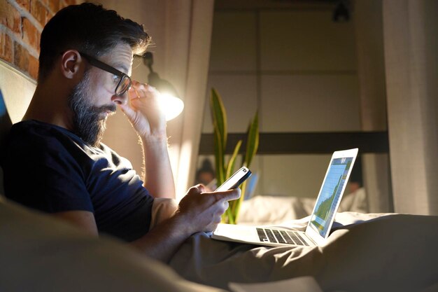 Vue latérale d'un homme avec des lunettes travaillant dans le lit la nuit