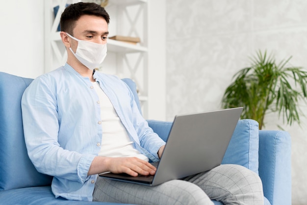 Photo vue latérale de l'homme à la maison avec masque médical travaillant sur ordinateur portable