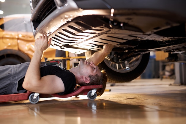 Vue latérale sur l'homme mécanicien automobile concentré travaillant seul sur le plancher de la réparation du bas de la voiture