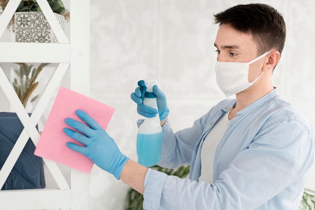 Photo vue latérale d'un homme nettoyant tout en portant un masque facial