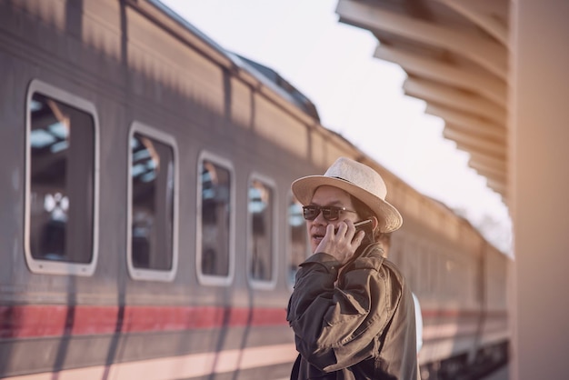 Photo vue latérale d'un homme parlant au téléphone portable debout près du train sur la plate-forme de la gare