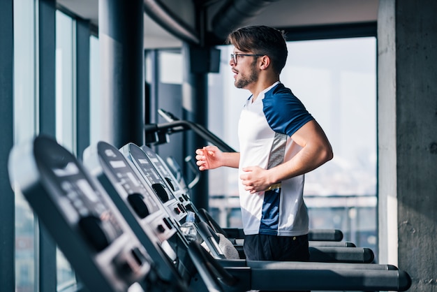 Vue latérale d&#39;un homme qui court dans la salle de sport moderne avec vue.