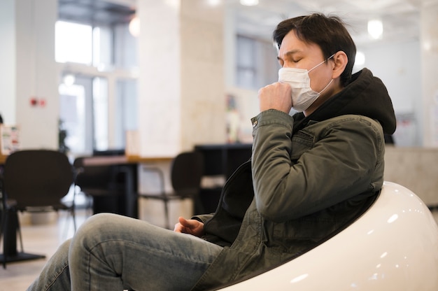 Vue latérale de l'homme se prélasser et tousser dans un masque médical