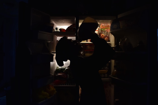 Photo vue latérale d'un homme en silhouette buvant debout près du réfrigérateur à la maison