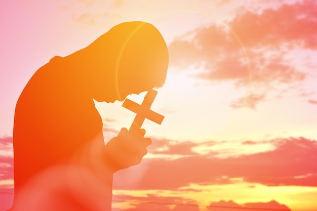 Vue latérale d'un homme en silhouette tenant une croix contre le ciel au coucher du soleil