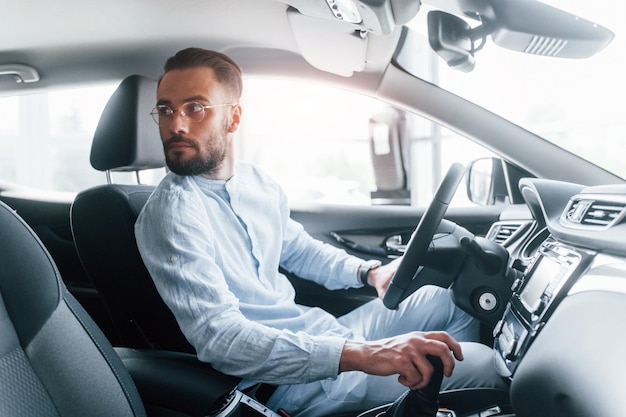 Vue latérale d'un jeune bel homme en vêtements formels assis dans une toute nouvelle automobile