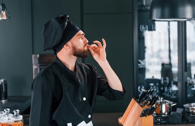 Vue latérale d'un jeune chef cuisinier professionnel en uniforme debout dans la cuisine