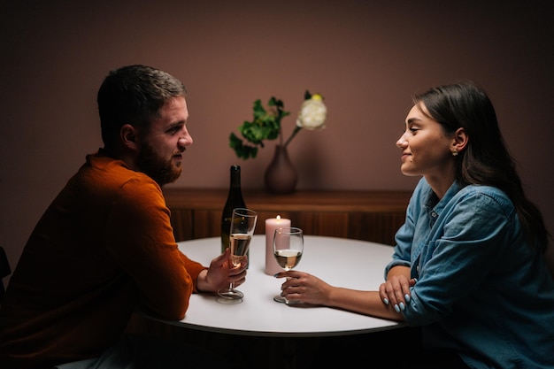 Vue latérale d'un jeune couple amoureux qui s'amuse à parler, à s'amuser ensemble, à célébrer la Saint-Valentin lors d'un dîner romantique, assis ensemble à une table de dîner avec une bougie dans un salon sombre et confortable.